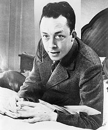 220px-Albert_Camus,_gagnant_de_prix_Nobel,_portrait_en_buste,_posé_au_bureau,_faisant_face_à_gauche,_cigarette_de_tabagisme.jpg